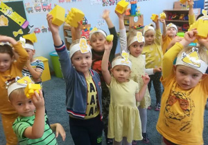 Dzieci stojąc pokazują znalezione w sali przedmioty w żółtym kolorze.